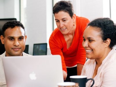 Two university students looking at laptop while lecturer looks over their shoulder. Image, UQ